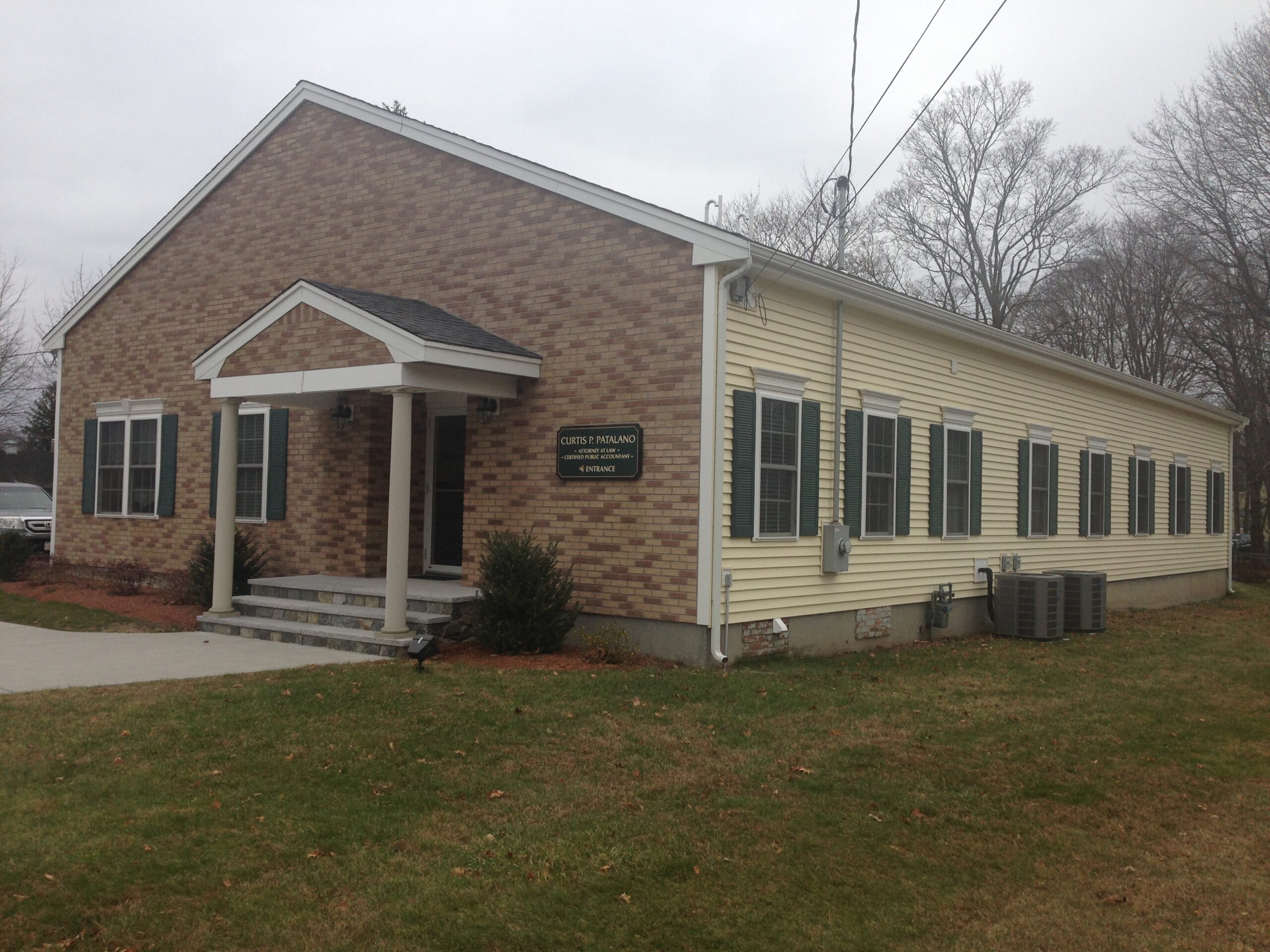 Curtis P. Patalano building exterior, featuring a brick and yellow siding façade, with a porch, green shutters, and a sign indicating the entrance.
