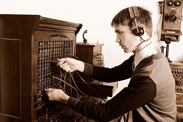 A telegraph operator connects wires on an early 20th-century switchboard, showcasing vintage communication technology and the labor of the era.